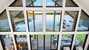 En modern inredning med stora fönster med utsikt över en sjö, en terrass med utomhusmöbler och en matplats.