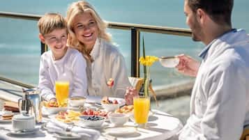 Une table à manger avec des aliments pour le petit-déjeuner, une vue sur la mer et une personne qui sert les plats.