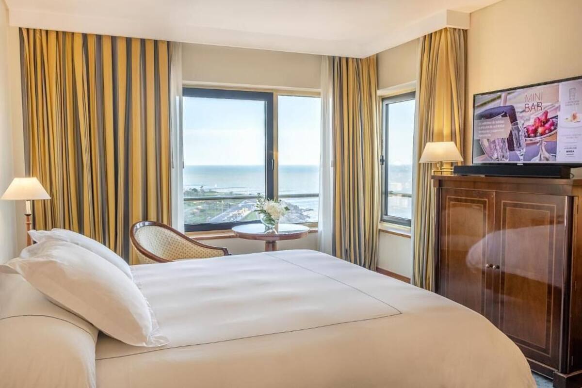 Een hotelkamer met een bed, een stoel, een tafeltje met een vaas, een televisie en uitzicht op zee.