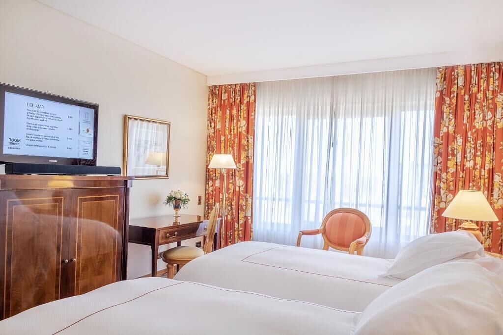 A hotel room with a bed, a desk, a television, and curtains.