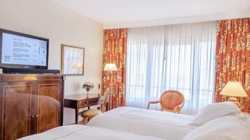 A hotel room with a bed, a desk, a television, and curtains.