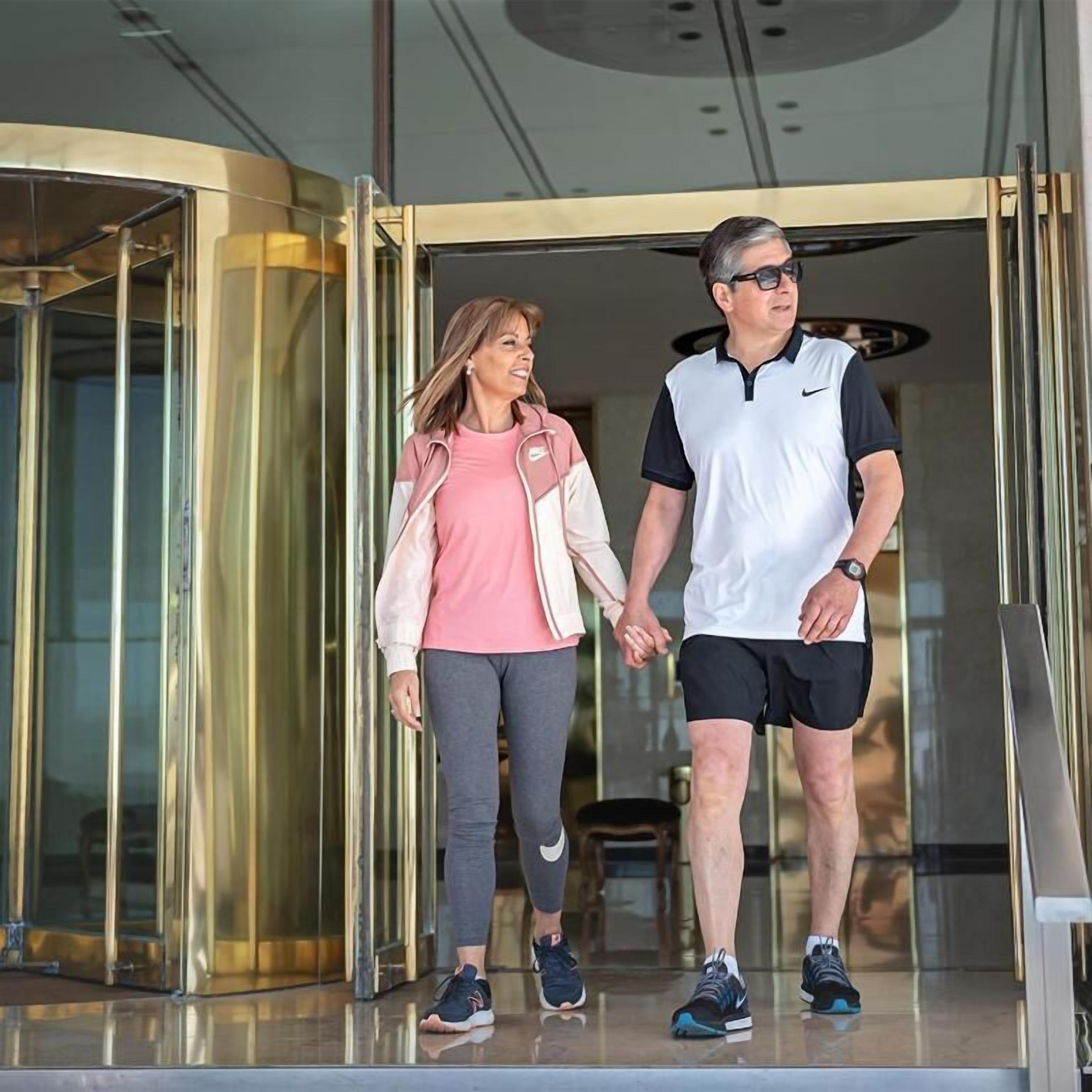 Um homem e uma mulher saindo de um edifício com entrada de vidro.