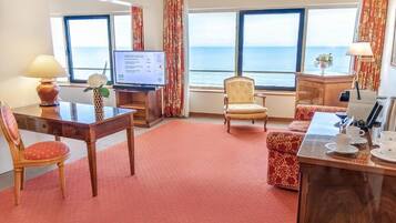 Quarto de hotel com escrivaninha, cadeira, sofá e vista para o mar.