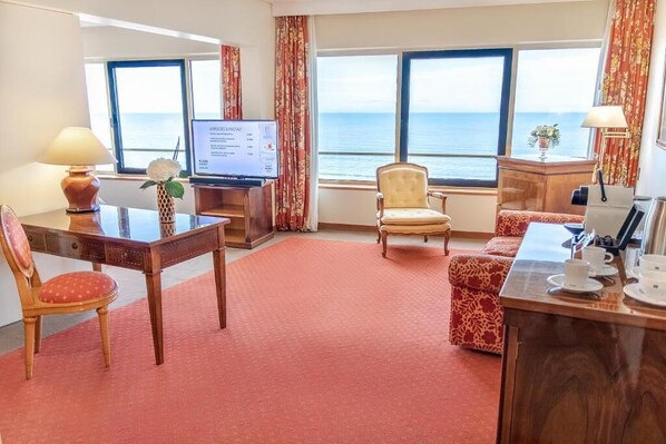 Ett hotellrum med ett skrivbord, en stol, en soffa och utsikt över havet.