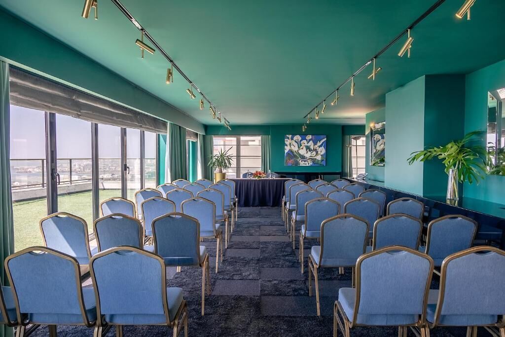 A conference room with rows of chairs, a table, and a painting on the wall.