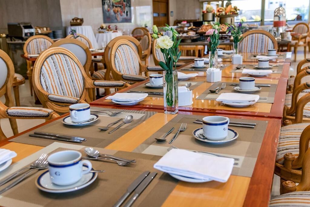 A dining area with tables set for service, chairs with striped upholstery, and a vase with flowers on the table.