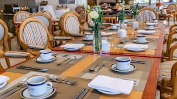 A dining area with tables set for service, chairs with striped upholstery, and a vase with flowers on the table.