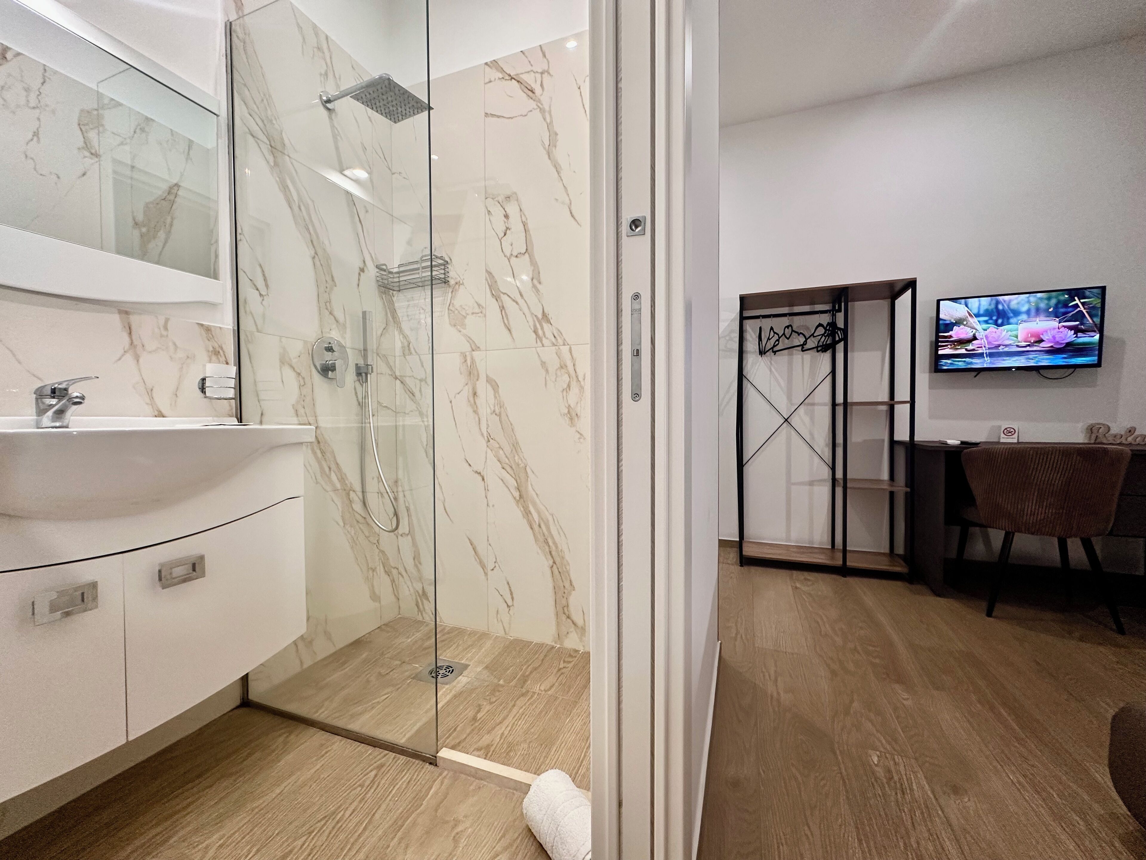 A modern bathroom with a glass-enclosed shower, a white sink, and a marble backsplash.