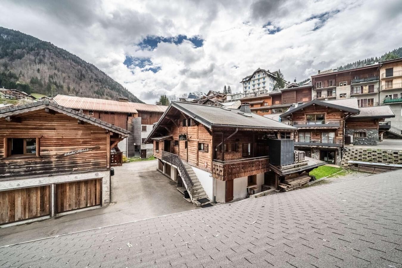 Ein traditionelles, holzverkleidetes Chalet mit Balkon, eingebettet in ein Bergdorf mit ähnlichen Häusern.