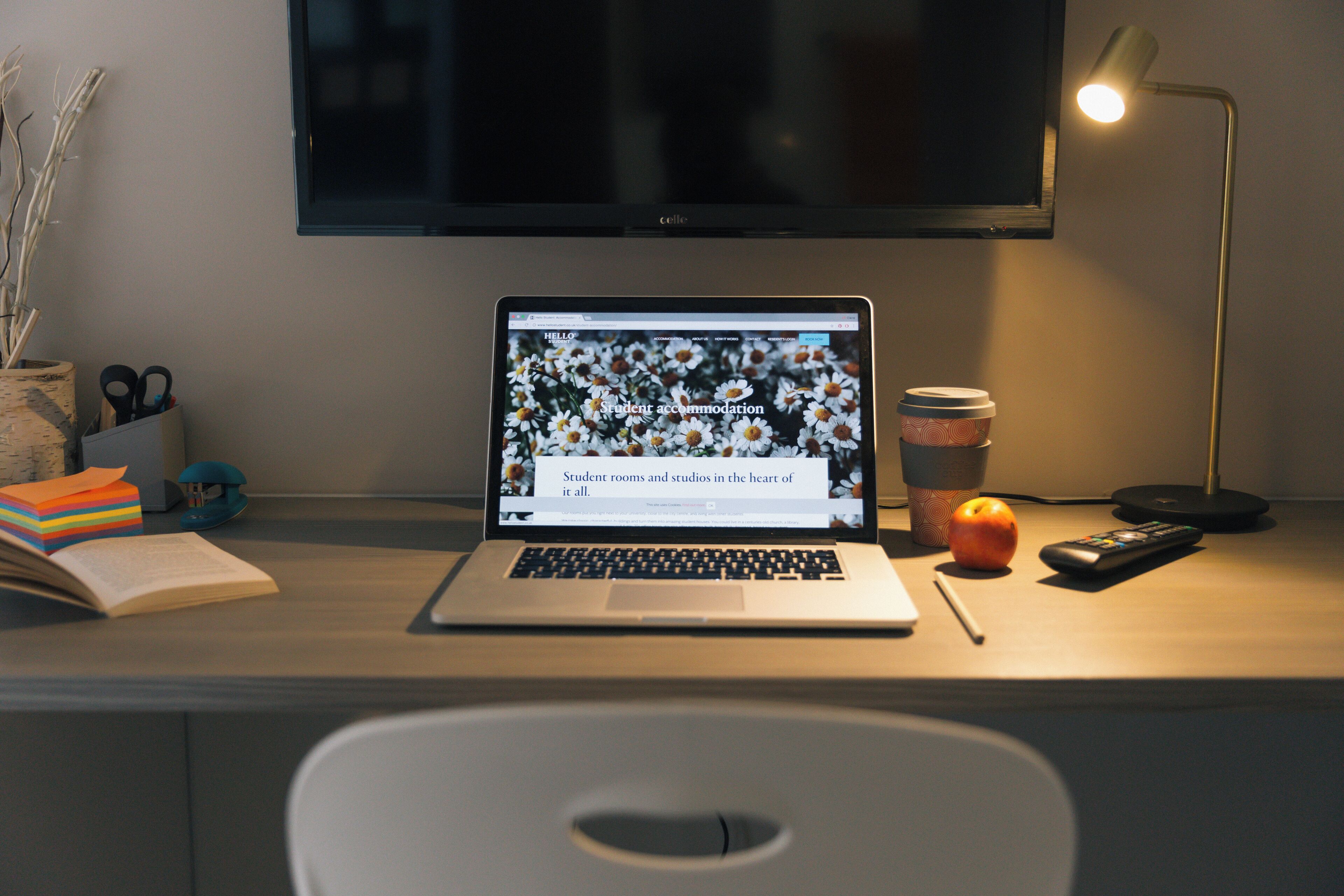 Un ordinateur portable sur un bureau, avec une tasse, une télécommande, une pomme et un livre.