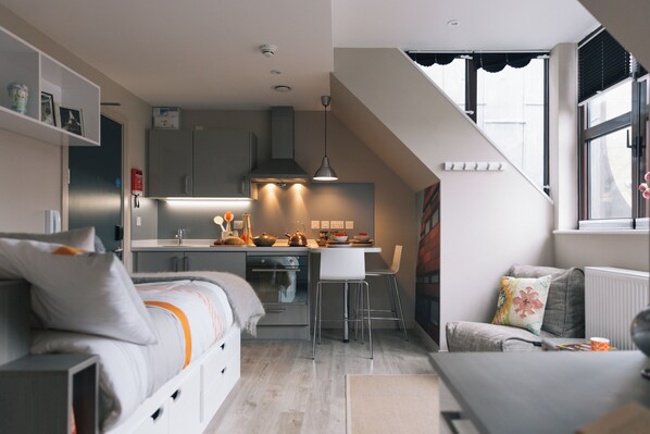 Une cuisine compacte dotée d’appareils électroménagers modernes, un coin repas avec des tabourets de bar et un espace salon confortable avec un canapé et un fauteuil.