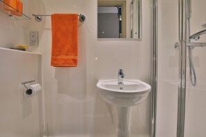 Une salle de bain avec un lavabo blanc, une cabine de douche en verre et une serviette orange accrochée au mur.
