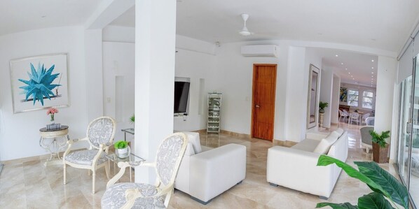 A spacious living area with a modern white sofa set, a decorative chair, and a glass coffee table. There is a large abstract painting on the wall and a television in the background. - Casa Romero Cartagena Club de Playa (Cartagena)