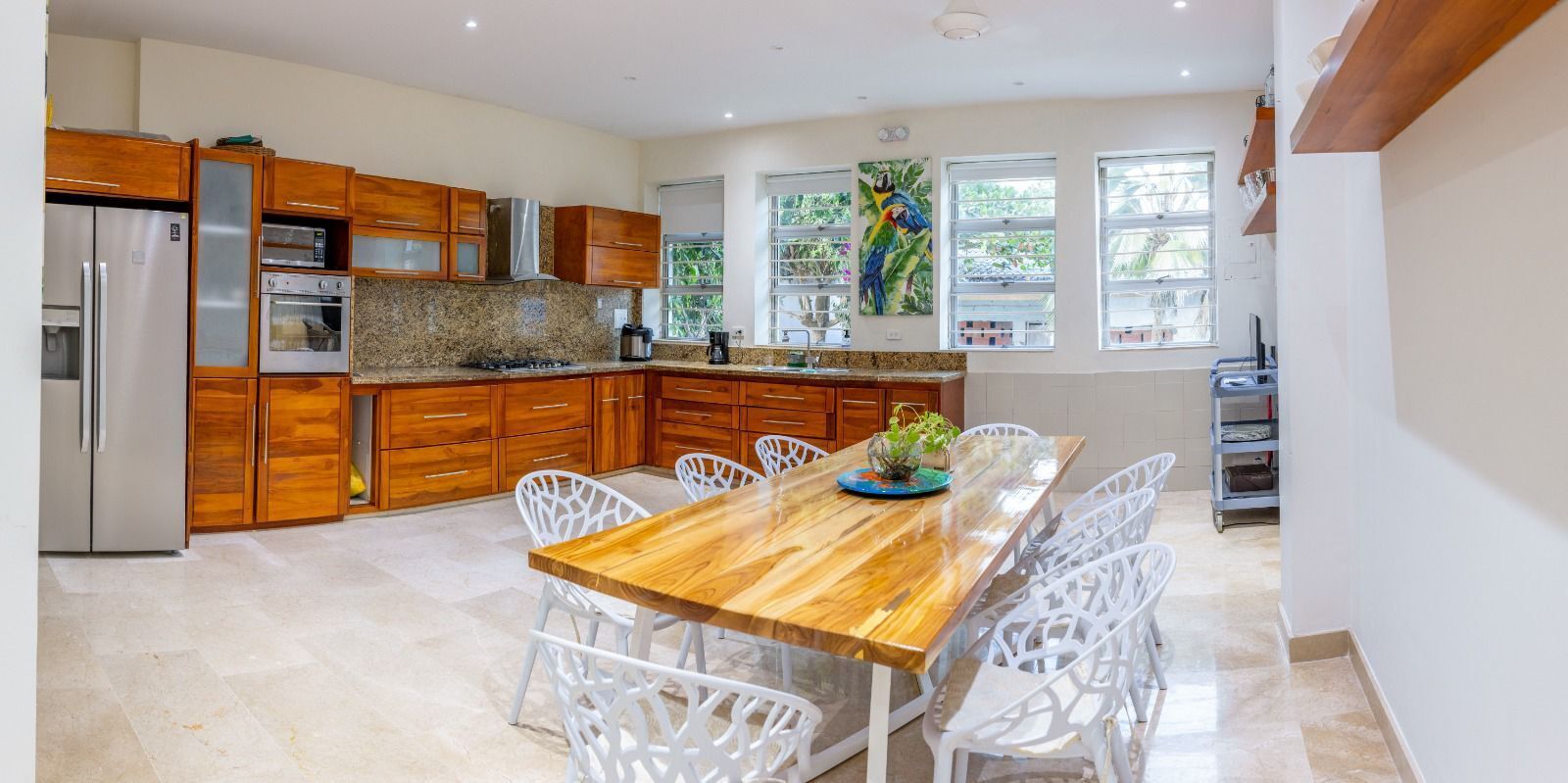 A modern kitchen with wooden cabinets, a granite countertop, and a dining area with white chairs.