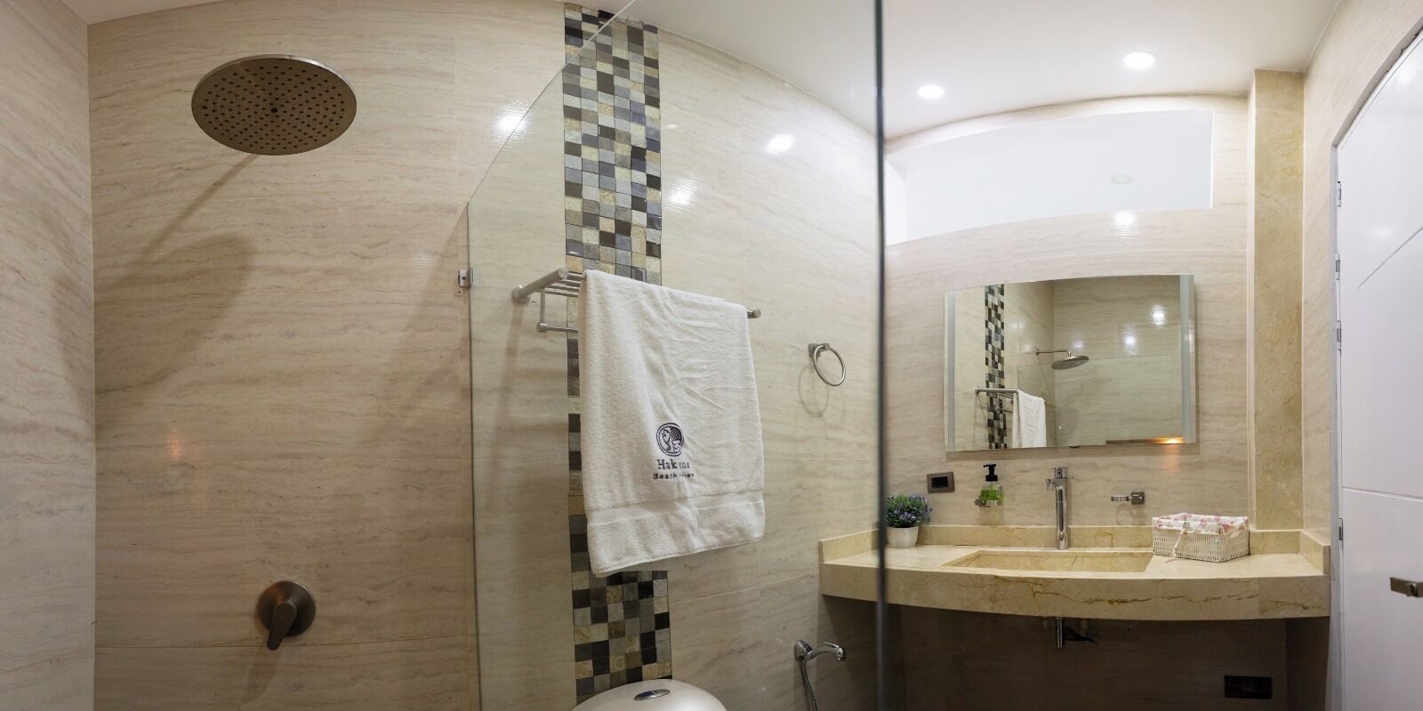 A modern bathroom with a glass shower enclosure, a marble-tiled wall, a sink with a mirror, and a towel hanging on a rack.