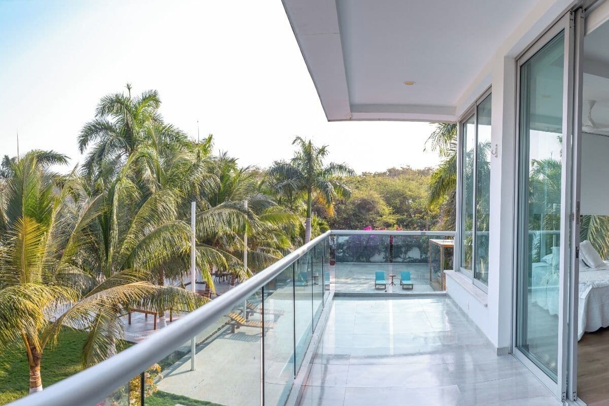 A modern room with a large glass balcony overlooking a lush garden and palm trees.