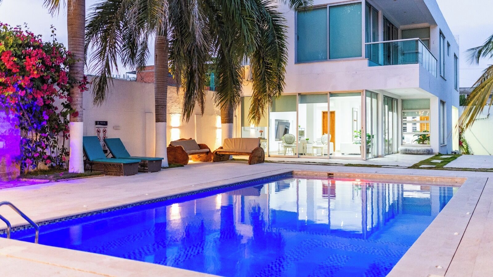Ein moderner Poolbereich mit klarem Wasser, Liegestühlen und einem Gebäude mit großen Fenstern und einem Balkon.