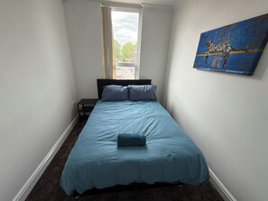 A small, neatly arranged bedroom with a single bed, a nightstand, and a window with curtains.