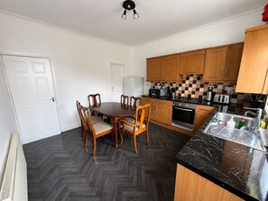 A kitchen with wooden cabinets, a dining table with chairs, a black marble countertop, and a herringbone floor pattern. - 3BR-Sleep 10– Near Stadium,Centre & M-Links - Contractors / Corporate & Families (Leeds)