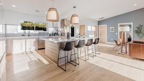 A modern kitchen with a central island, bar stools, pendant lighting, and a view of the outdoors.