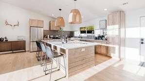 A modern kitchen with a large island, pendant lighting, and a view of the outdoors. - Sauna & Cold Plunge Cabin + Mountain Wellness Retreat (Bryson City)