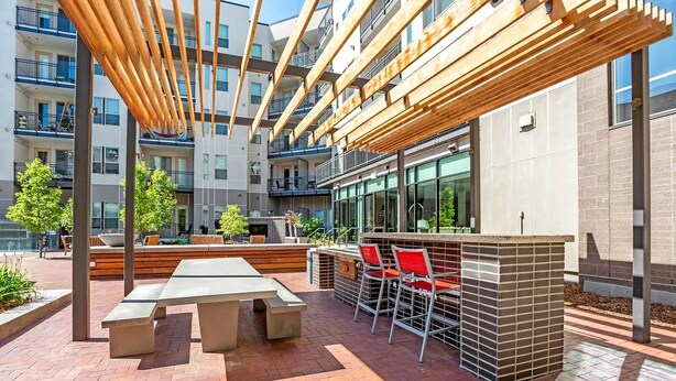 An outdoor patio with a wooden pergola, a long table, and red chairs. - Landing | Beautiful Studio, Gym, Rooftop Lounge (Denver)