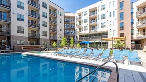 A swimming pool with lounge chairs, surrounded by multi-story buildings with balconies. - Landing | Beautiful Studio, Gym, Rooftop Lounge (Denver)