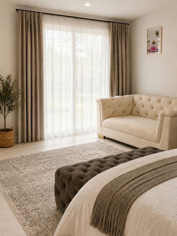 Une chambre avec un canapé beige, un pouf capitonné, un tapis à motifs et une plante en pot.