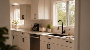 A modern kitchen with white cabinets, stainless steel appliances, a black faucet, and a window with a view of trees.