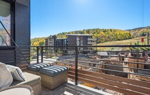 A balcony with wicker furniture, a view of a construction site, and buildings in the background. - Charlie's Slopeside: Ski-In/Out, Sleeps 7, Snowmass Base Village, Pool + Waterslide, Walk to Dining (Snowmass Village)
