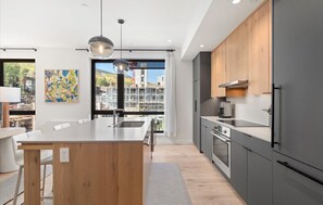 A modern kitchen with a central island, grey cabinets, and a view of a cityscape through large windows. - Charlie's Slopeside: Ski-In/Out, Sleeps 7, Snowmass Base Village, Pool + Waterslide, Walk to Dining (Snowmass Village)