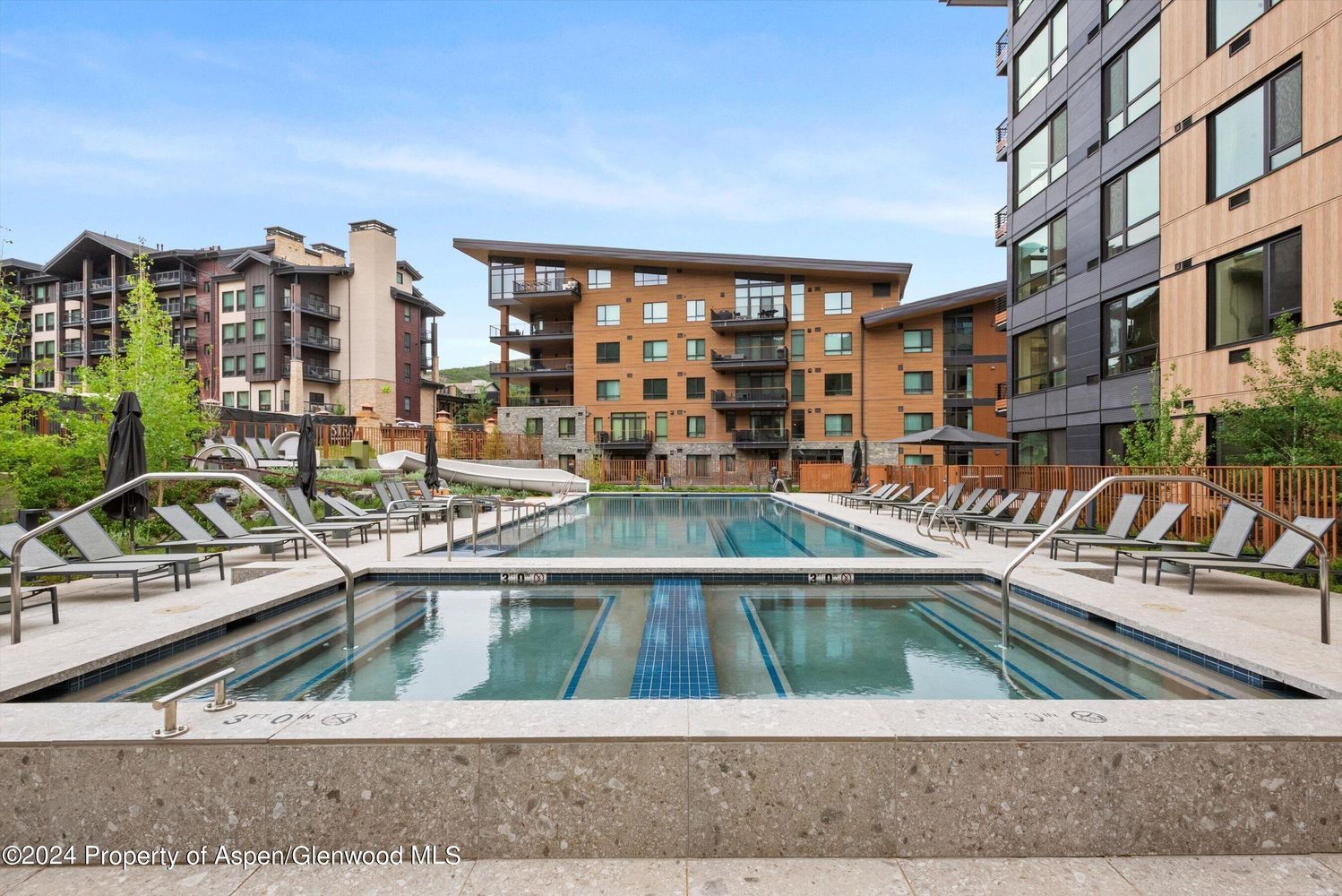 A swimming pool with lounge chairs and a modern building complex in the background.