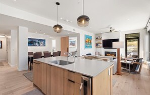 A modern kitchen with a central island, pendant lighting, and a dining area with chairs.