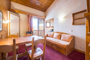 A cozy room with a wooden table and chairs, a sofa, and a sliding glass door leading to a balcony. - Resort center, 4th floor, balcony, 28m², La Plagne (La Plagne)