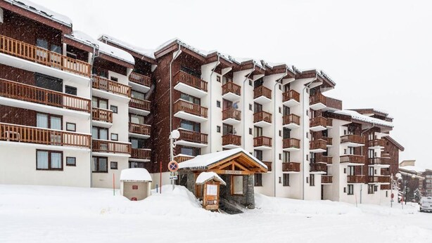 Un hôtel à plusieurs étages doté de balcons, d’un télésiège et d’un petit bâtiment en bois.