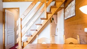 Un escalier en bois mène à une chambre à coucher où l’on aperçoit un lit et, au fond, une salle de bain.