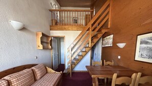 Une pièce chaleureuse avec un escalier en bois, un canapé, une table à manger et des chaises.
