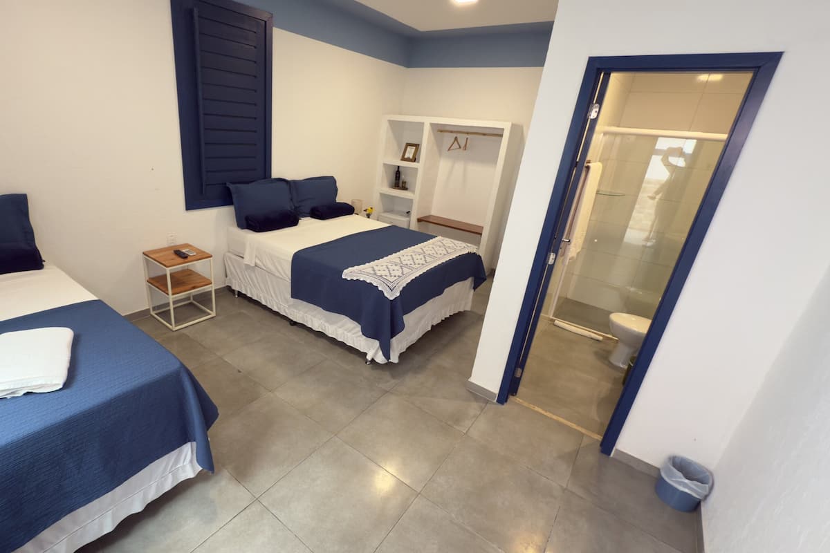 Een hotelkamer met twee bedden, een klein nachtkastje met een telefoon, een andere nachtkastje met een lamp, en een badkamer zichtbaar door een geopende deur.