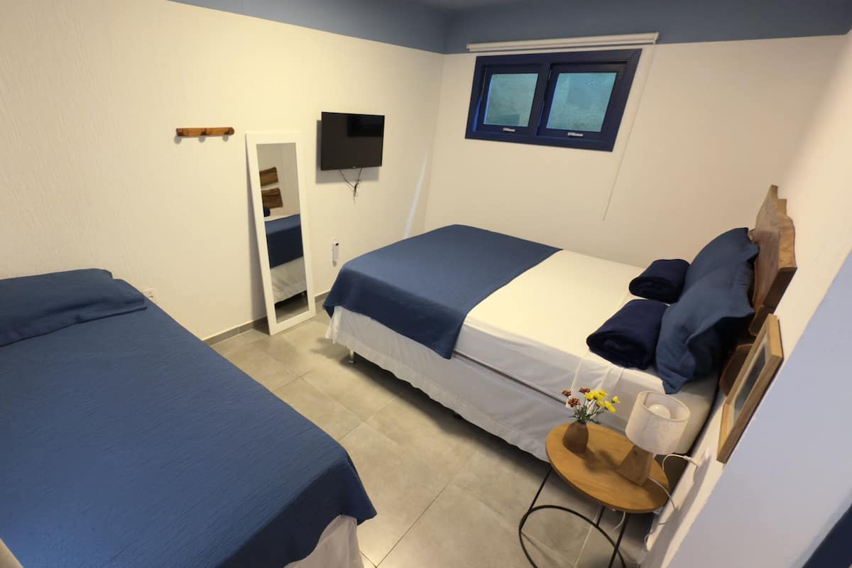 Een kamer met twee bedden, een aan de muur bevestigde televisie, een raam en een klein tafeltje met een vaas.