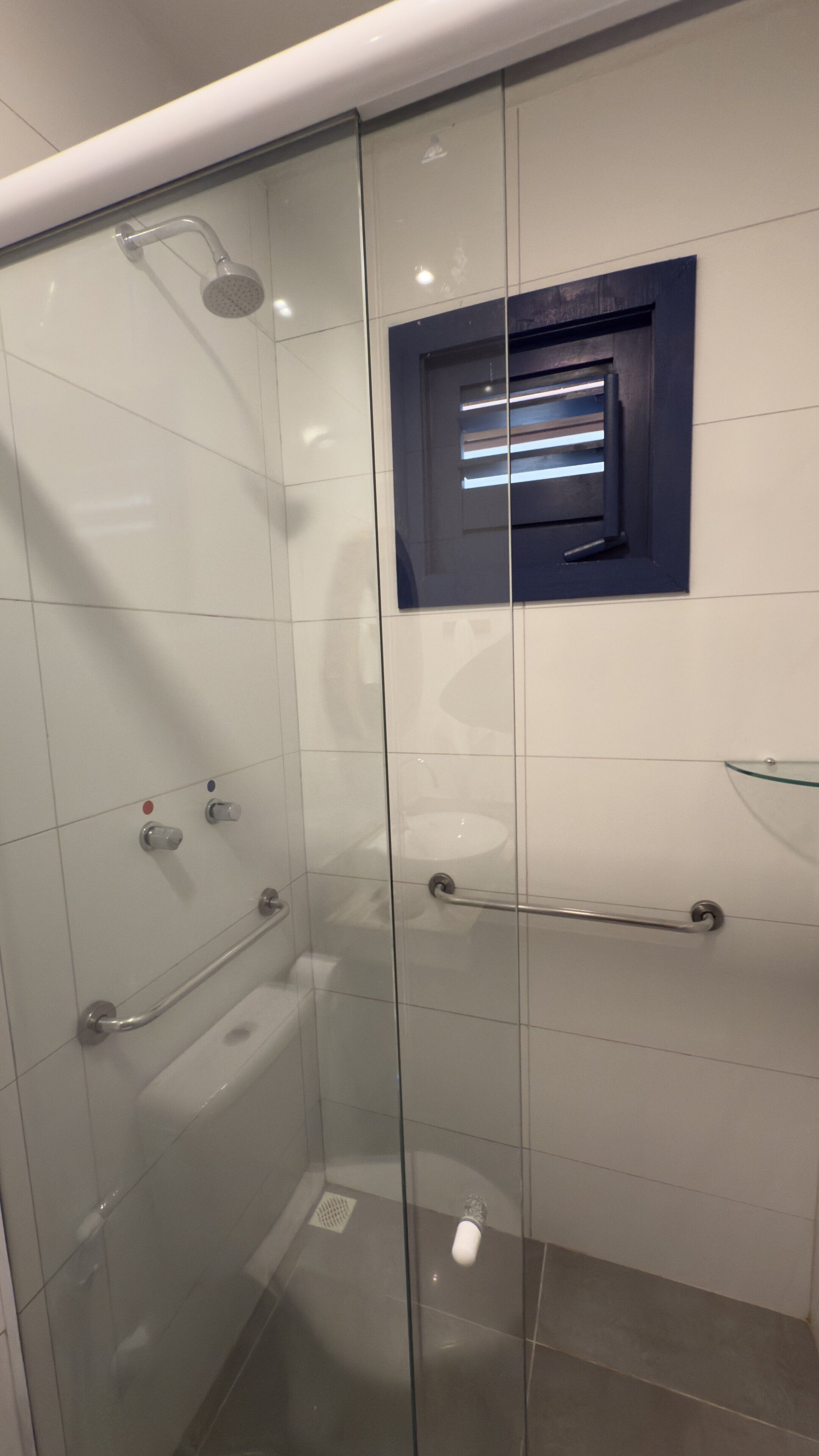 Ein modernes Badezimmer mit Duschkabine aus Glas, Waschbecken mit Glasausführung und einem kleinen Fenster über dem Waschbecken.