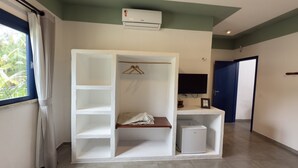 Une pièce avec une armoire blanche, une petite table, un climatiseur blanc, un téléviseur et une porte.