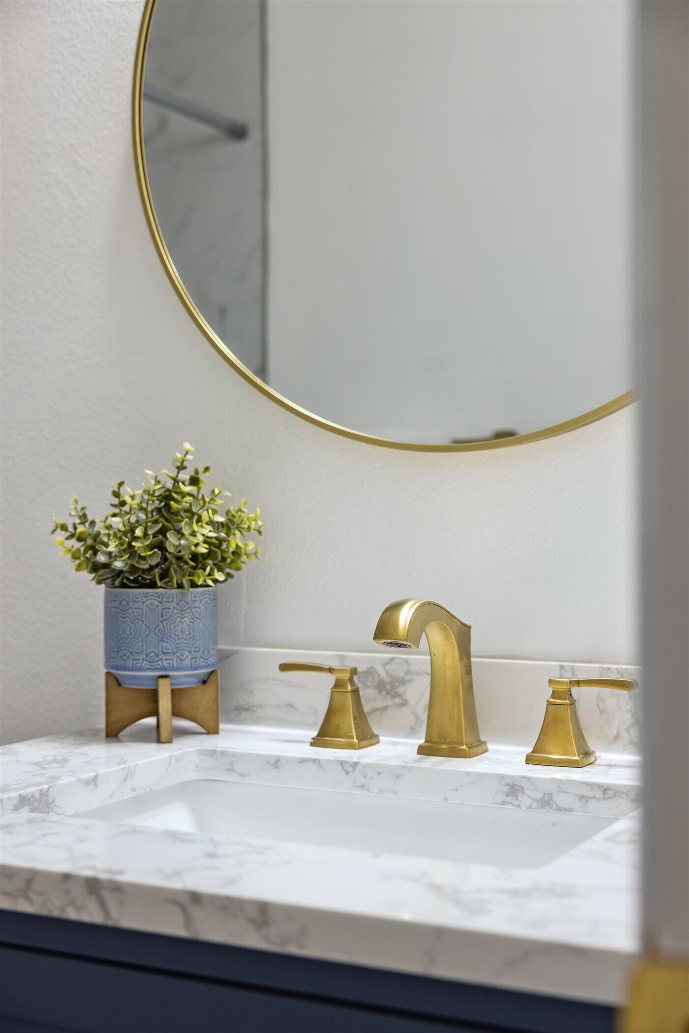 Un baño con lavamanos de mármol, grifos dorados y una planta en maceta.