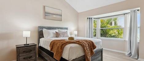 A bedroom with a bed, nightstand, ceiling fan, and large window with curtains.