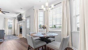 A modern dining area with a round table, grey upholstered chairs, and a chandelier. - Spacious 5BR Retreat Sleeps 14 Huge Yard! (Warner Robins)