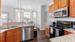 A modern kitchen with wooden cabinets, stainless steel appliances, a dishwasher, and a granite countertop. - Spacious 5BR Retreat Sleeps 14 Huge Yard! (Warner Robins)