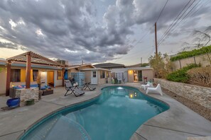 Un patio trasero con piscina, sillas de descanso, una pérgola y una zona de patio.