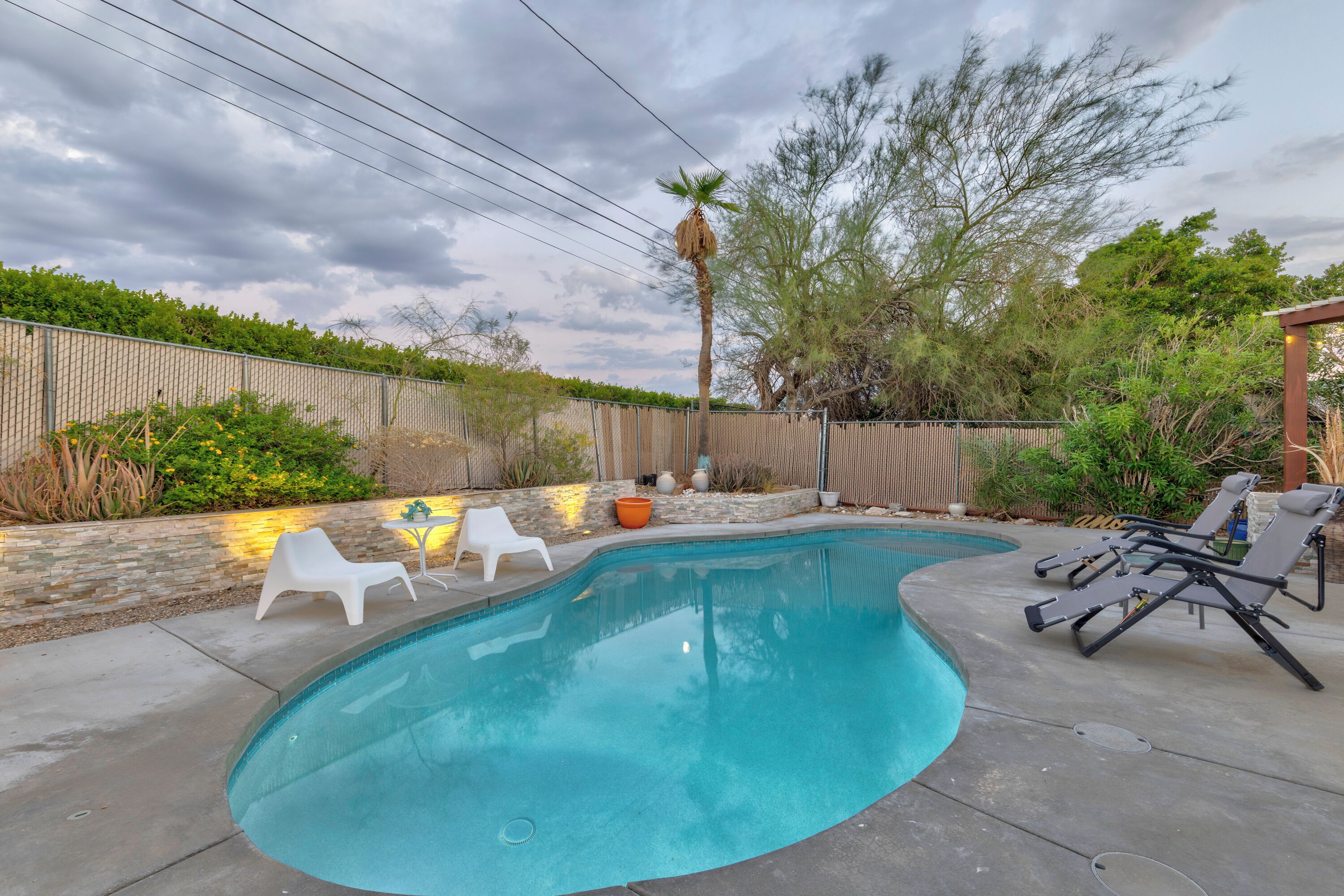 A backyard with a swimming pool, white lounge chairs, and a wooden pergola.