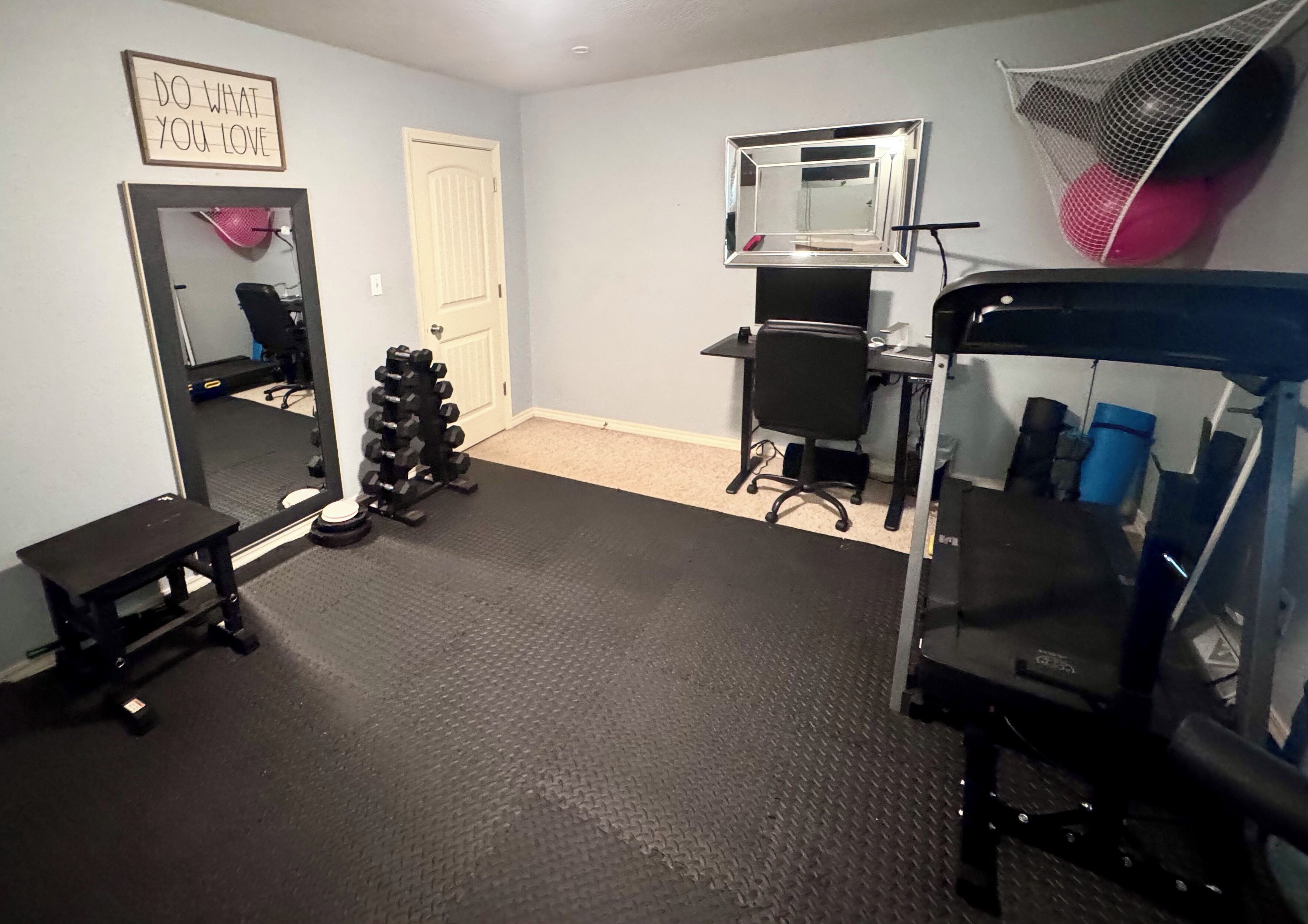 A home gym with a mirror, weight rack, bench, and exercise equipment.