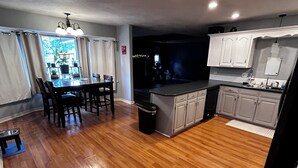 A modern kitchen with wooden flooring, a dining area with a table and chairs, and a view of the outdoors through large windows. - Roomy 4-bed house in Springfield + Pet friendly + Gym + Workspace (Springfield)