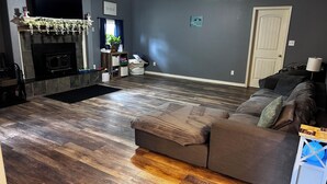 A living room with a wooden floor, a fireplace, a couch, and a television. - Roomy 4-bed house in Springfield + Pet friendly + Gym + Workspace (Springfield)